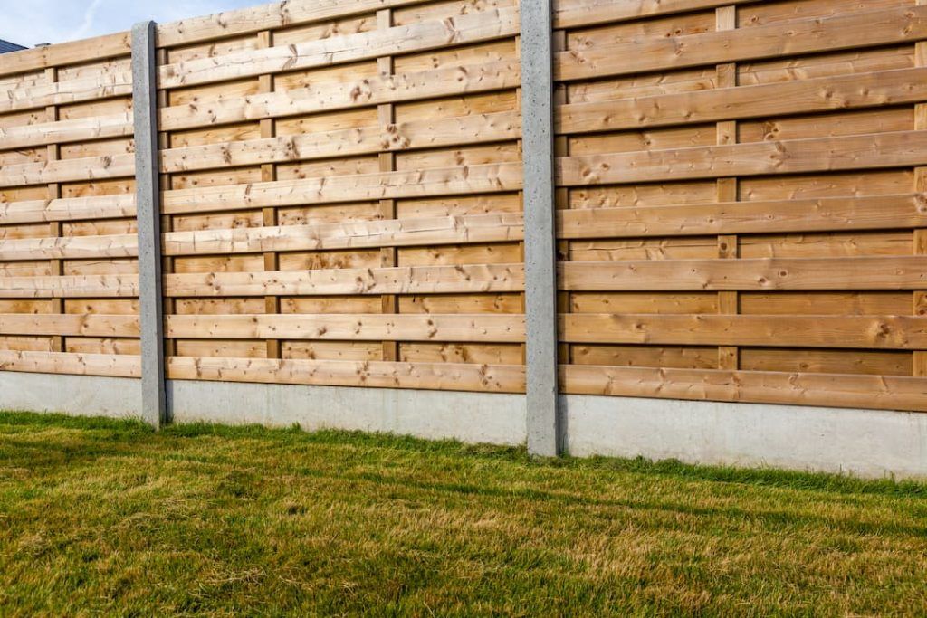 a wooden fence with concrete pillars and grass